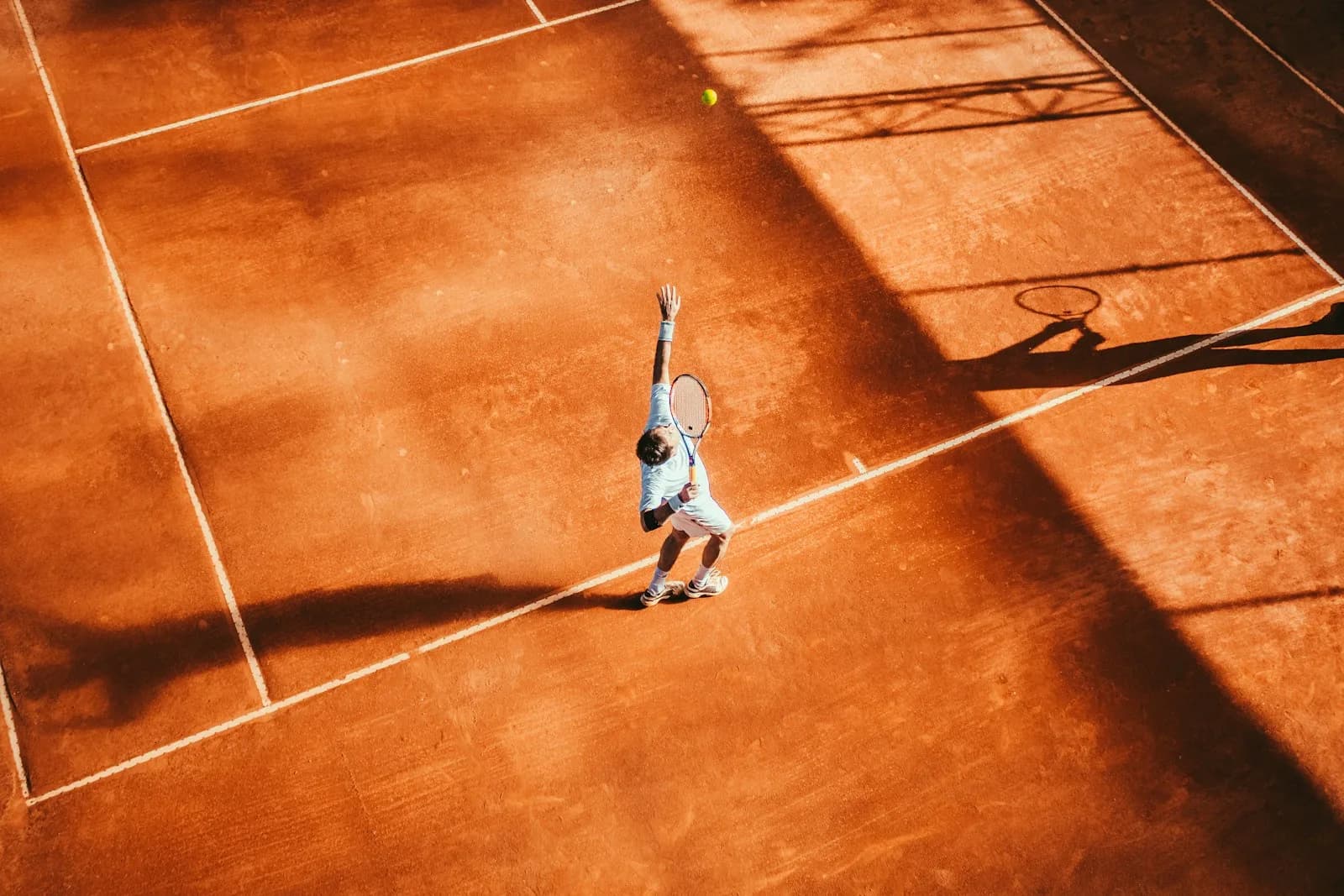 Jugador de tenis sacando en una pista de tierra batida, vista cenital